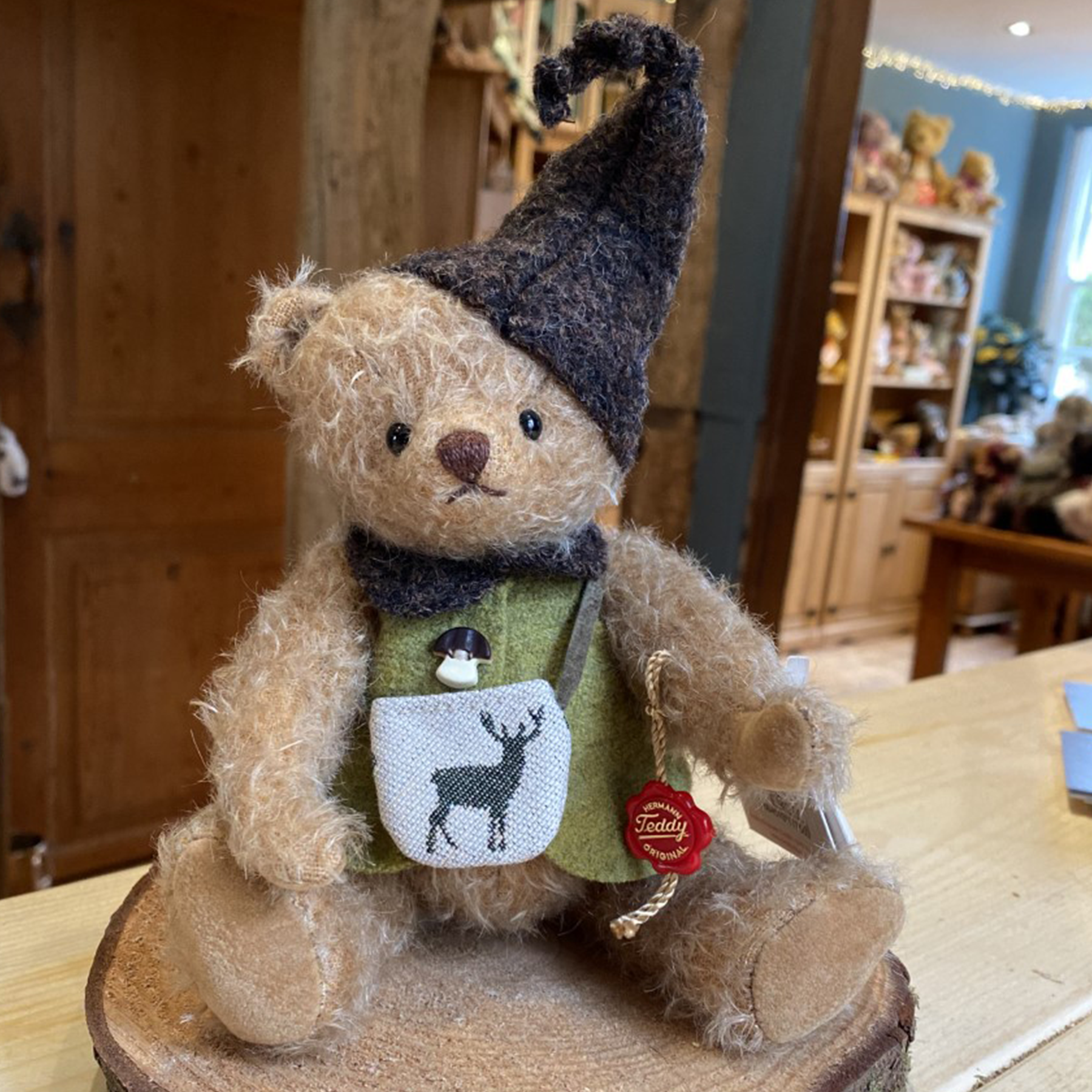 This little forest teddy stands at 20cm and is made from sparse distressed mohair.  Wearing a green jacket closed with a wooden mushroom button and carrying a shoulder bag with reindeer motif.  A brown pointed hat and matching collar finish this little ones outfit.  Limited to 200 pieces worldwide