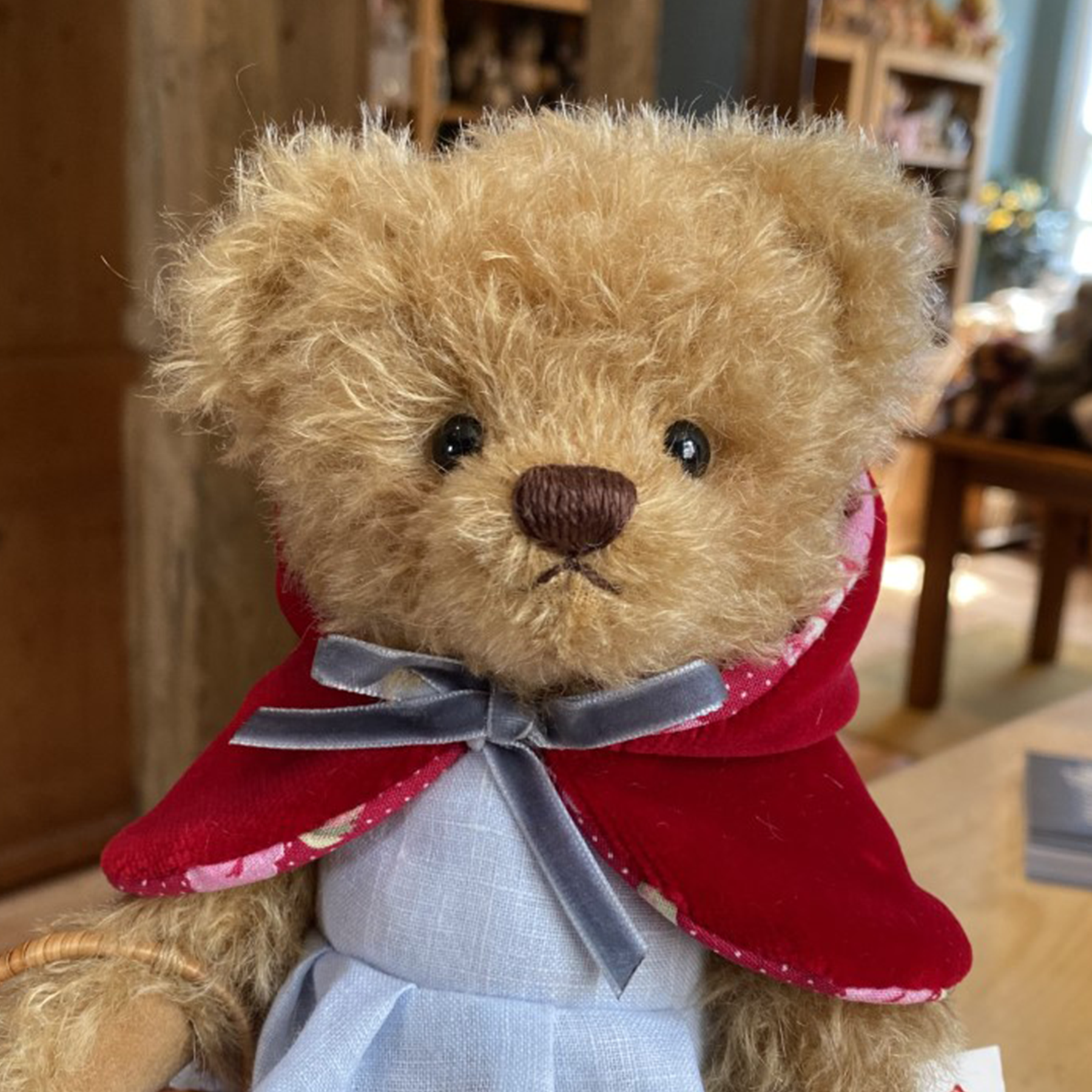 Little Red Riding Hood is beautifully soft and made from slightly wavy caramel coloured mohair. Her flat footpads allow her to stand on her own.  She is wearing a striking red velvet lined cape and a pretty blue linen dress she carries a fabric lined wicker basket